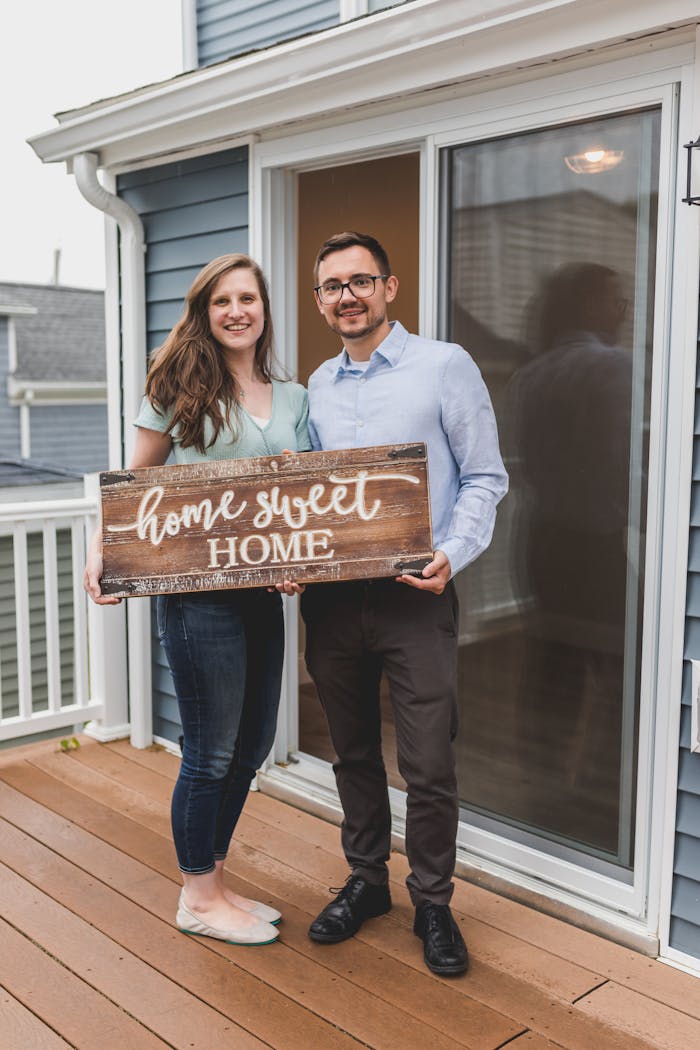 Smiling couple holding Home Sweet Home sign in front of their new house.