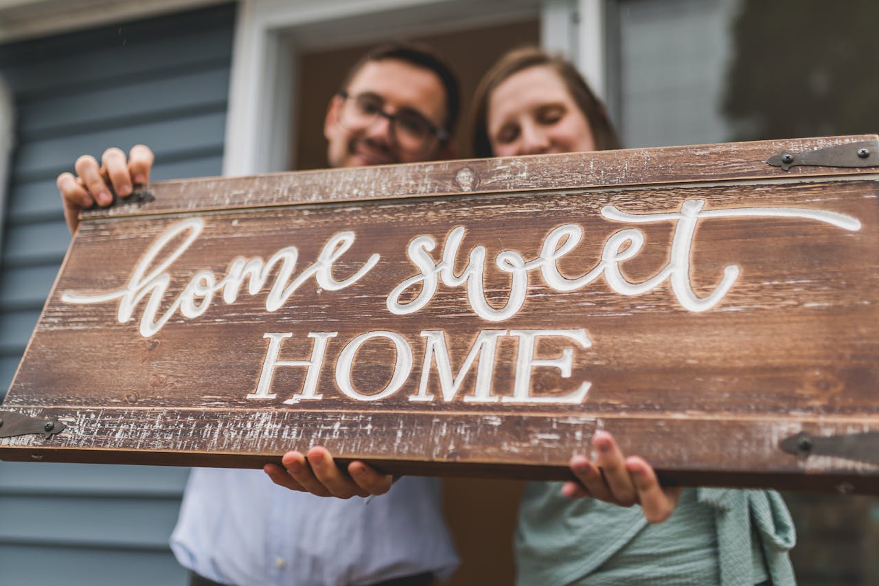 A joyful couple holding a home sweet home sign in front of their new house.